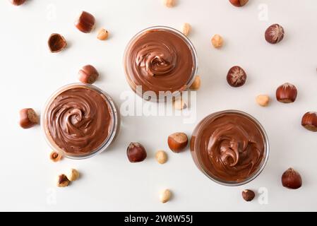 Cocoa cream in glass bowls with hazelnuts around on white table. Top view. Stock Photo