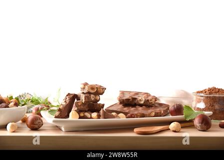 Freshly made chocolate with hazelnuts on a white plate with ingredients around on a wooden table with white isolated background. Front view. Stock Photo