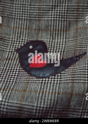 Vertical straight from above shot of a woman’s plaid shoulder bag detail - a brown leather bird with a red heart. Stock Photo