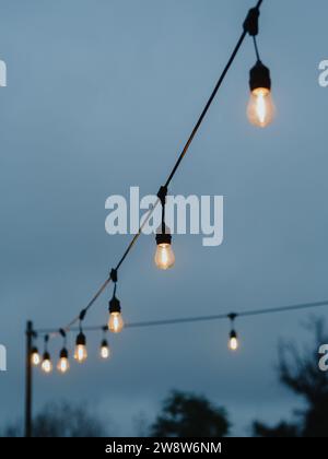 Vertical directly below shot capturing two strings of light bulbs against the backdrop of a grey, cloudy dusk sky. November in Warsaw, Poland. Stock Photo
