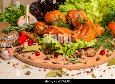 Smoked chicken legs with fresh herbs, garlic, slices of rye bread, tomatoes and other seasonings on a cutting board Stock Photo