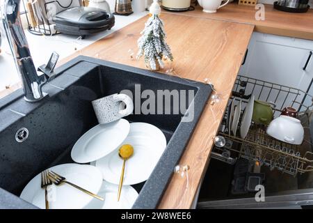 Dirty dishes in the sink in the garlanded kitchen, a holiday after a feast at Christmas. Mess after the guests for the New Year, kitchen cleaning, det Stock Photo