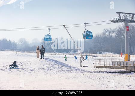Bansko, Bulgaria - December 20, 2023: Bulgarian winter ski resort panorama with gondola lift cabins, Pirin mountain peaks view and people near lower s Stock Photo