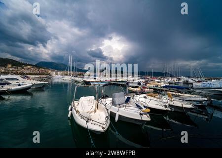 Motorboats and sailing boats at anchor in the Santa Teresa marina in Salerno, the city's buildings in the distance and dark storm clouds gathering. Stock Photo