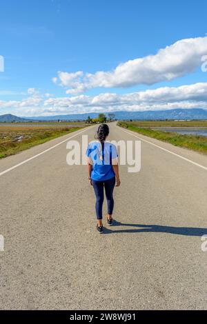 View from behind of Latina woman walking along a deserted highway Stock Photo