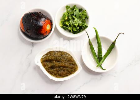 Homemade roasted tomato sauce or chutney served in a small ceramic dish on white background along with ingredients roasted tomato, green chilli. Stock Photo