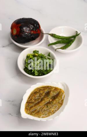 Homemade roasted tomato sauce or chutney served in a small ceramic dish on white background along with ingredients roasted tomato, green chilli. Stock Photo
