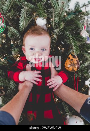 Smiling Baby being held up against christmas Tree Stock Photo