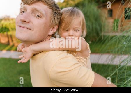 Father gives his happy daughter piggyback rides in the backyard Stock Photo