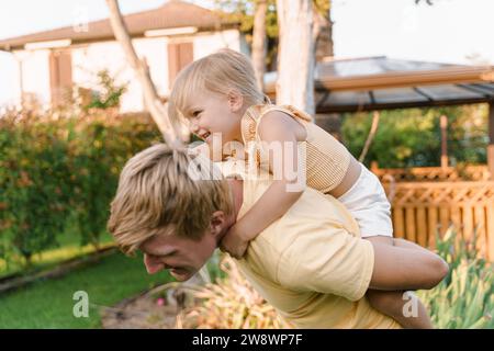 Father gives his happy daughter piggyback rides in the backyard Stock Photo