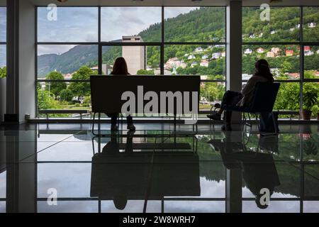 Bergen, Norway, June 29, 2023: Silhouette of two unidentifiable women look outside a large window of the Bergen cityscape while sitting on furniture i Stock Photo
