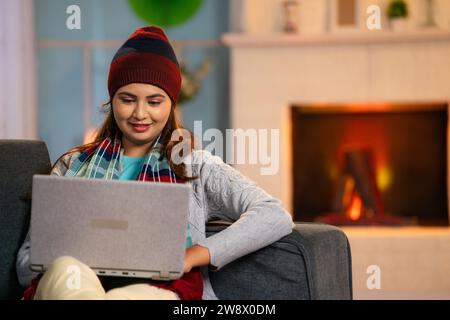 Happy warmth Woman with winter wear using or working on laptop at home on sofa - concept of freelancer, workplace and freedom Stock Photo