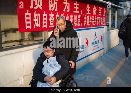 Chinese father pushes his sick son in wheelchair while talking on his mobile phone in a hospital in Beijing, China. 22-Dec-2023 Stock Photo