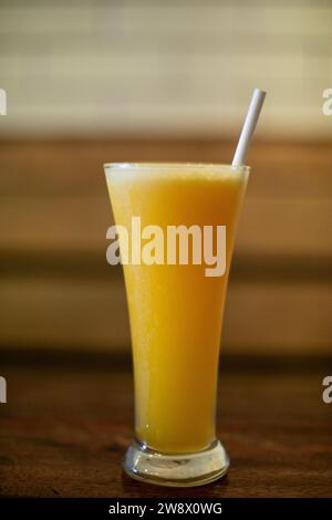 A close-up photo of a glass of orange juice with a single, bendy straw. The glass is tall and cylindrical, and the juice is a vibrant orange color, pu Stock Photo