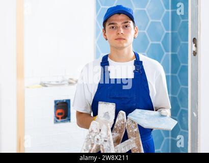 Construction worker in work clothes engaged in wall tiling work during overhauls indoors Stock Photo