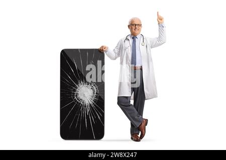 Doctor leaning on a smartphone with a cracked screen and pointing up isolated on white background Stock Photo