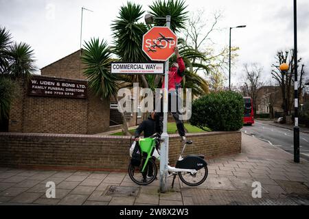 A person removes a piece of art work by Banksy, which shows what looks like three drones on a traffic stop sign, which was unveiled at the intersection of Southampton Way and Commercial Way in Peckham, south east London. Picture date: Friday December 22, 2023. Stock Photo