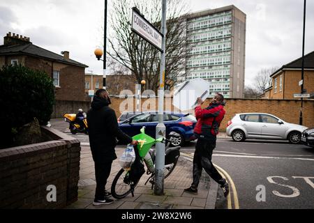 A person removes a piece of art work by Banksy, which shows what looks like three drones on a traffic stop sign, which was unveiled at the intersection of Southampton Way and Commercial Way in Peckham, south east London. Picture date: Friday December 22, 2023. Stock Photo