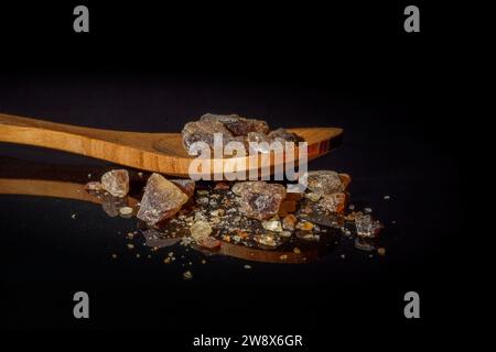 Close-up of brown rock sugar on a wooden spoon with a black background, diabetic concept, with copy space Stock Photo