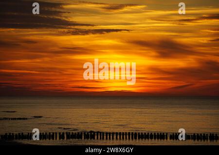 The photo depicts a sunset over the Baltic Sea, with the sky painted in shades of orange and adorned with scattered clouds. Sunset in Germany. Stock Photo