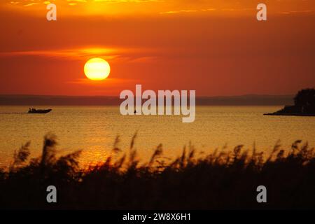 A pretty sunset over the Baltic Sea: the sun's bright orange colors fill the sky. There's a small boat in the sunlight on the calm sea. Gulf of Gdansk Stock Photo