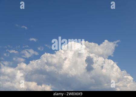 A large, pure white cumulus cloud, resembling a colossal mountain, set against the backdrop of a clear blue sky Stock Photo