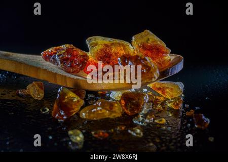 Close-up of brown rock sugar on a wooden spoon with a black background, diabetic concept, with copy space Stock Photo
