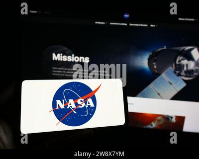 Person holding cellphone with logo of American National Aeronautics and Space Administration (NASA) in front of webpage. Focus on phone display. Stock Photo