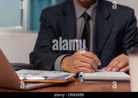 Businessman working at office with laptop and documents analyzing graphs and taking notes on desk. Business holding pen and paper notes chart marketin Stock Photo