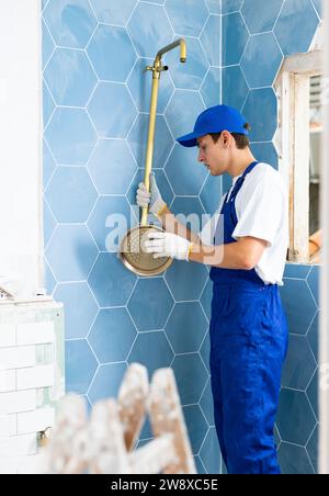 Focused young plumber installing shower in apartment under renovation Stock Photo