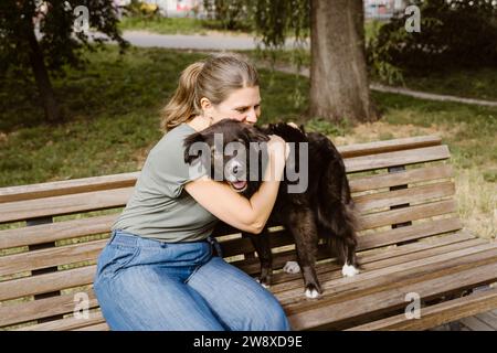 Mature woman embracing dog on bench in park Stock Photo