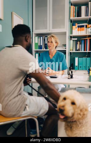 Young man with dog talking to female veterinarian at desk in medical clinic Stock Photo