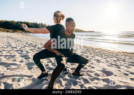 Determined man doing squats with woman on sand at beach Stock Photo