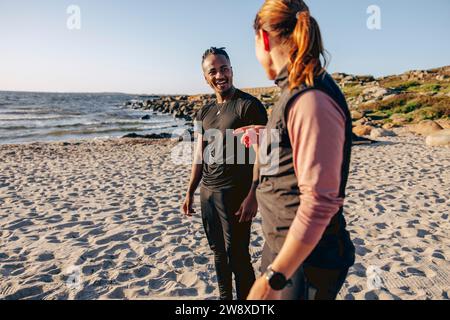 Side of woman talking with young man while standing on sand during group training session at beach Stock Photo