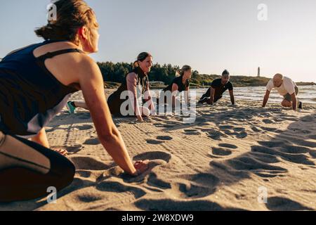 Smiling female instructor doing stretching with team on sand at beach Stock Photo