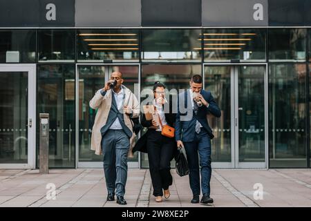 Full length of male and female business colleagues having food while walking in front of office building Stock Photo