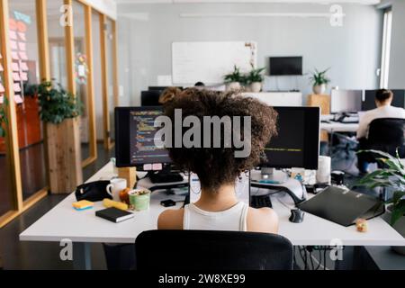 Rear view of female computer programmer sitting at desk in office Stock Photo