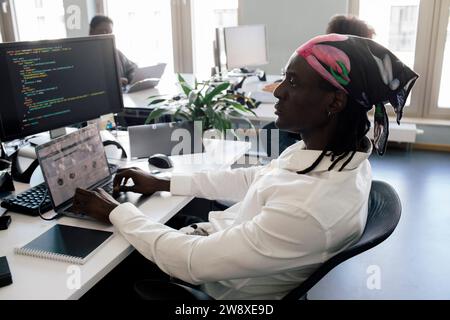Concentrated male computer programmer working on laptop while sitting at desk in office Stock Photo