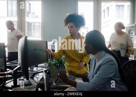 Businesswoman explaining coding to female colleague sitting at desk in office Stock Photo