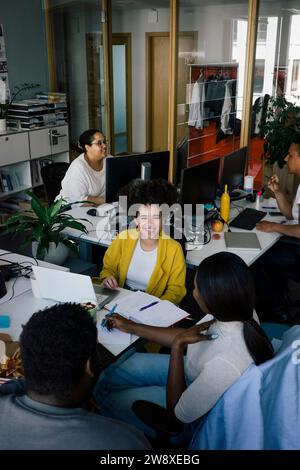 Happy female colleague discussing with coworkers at office Stock Photo