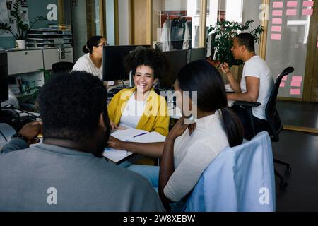 Happy female colleague talking with colleagues working at office Stock Photo
