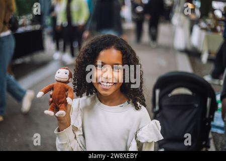 Portrait of happy girl holding toy monkey at flea market Stock Photo