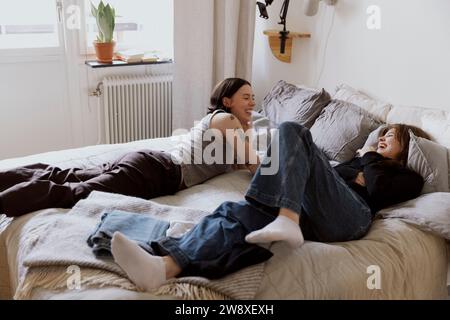 Happy female friends having fun while lying on bed in apartment Stock Photo