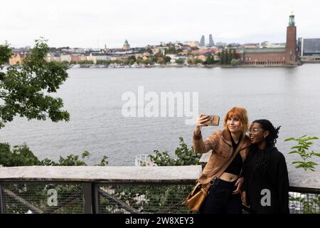 Woman talking selfie with female friend through smart phone near sea on vacation Stock Photo