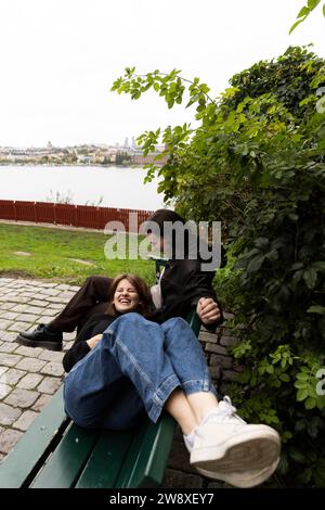 Happy woman lying down on lap of female friend sitting on bench at park Stock Photo
