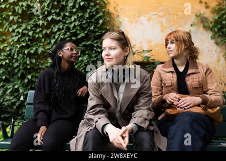 Young woman looking away while sitting with female friends on bench at park Stock Photo