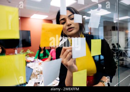 Businesswoman writing on adhesive note during brainstorming session at office Stock Photo
