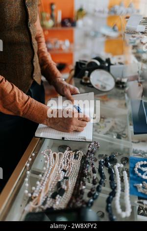 Midsection of male entrepreneur writing in diary while standing at store Stock Photo