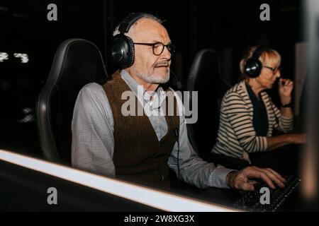Senior man wearing headset playing video game on computer by female friend at gaming center Stock Photo