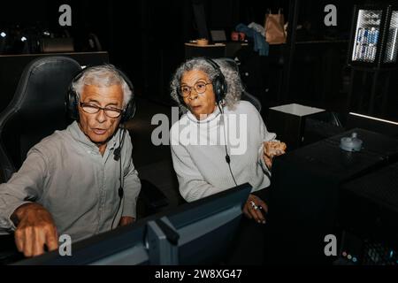Senior woman looking at computer while male friend playing video game in gaming center Stock Photo